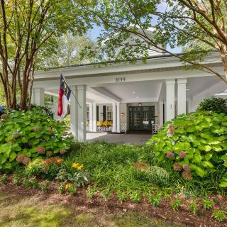 A building entrance surrounded by lush greenery and a flag displayed.