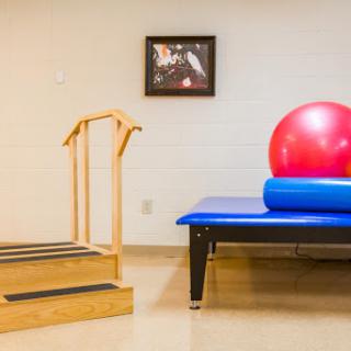 A rehabilitation space featuring a staircase for balance training, a blue treatment table, and a red exercise ball.