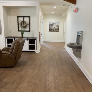 A hallway with wooden flooring, featuring a recliner and decorative items.