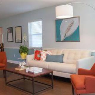A modern living room with a beige sofa, orange armchairs, and contemporary artwork on the wall.