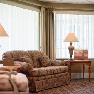 A cozy living room with a plush armchair, side table, and lamps by large windows with curtains.