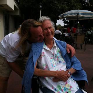 A tender moment shared between two people as one leans in to hug the other, who is seated in a wheelchair.