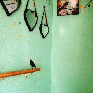 A cozy room corner with heart-shaped mirrors, a bird figurine on a wooden ledge, and a serene artwork against green walls.