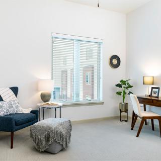 A minimalist living room with a cozy reading chair, desk area, and abundant natural light from the window.