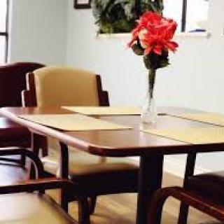 A dining table with a vase of red flowers.