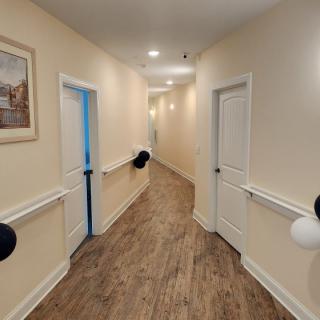 A well-lit hallway with wooden floors and multiple doors, adorned with wall-mounted artwork.