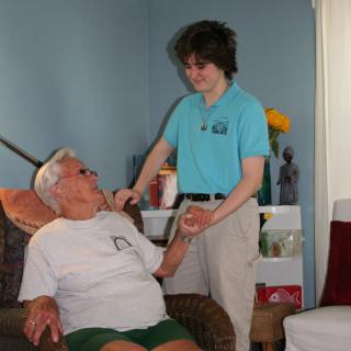 A caregiver assisting an elderly person in a living room setting.