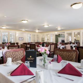 A well-arranged dining room with tables set for a meal, featuring red napkins and floral centerpieces.