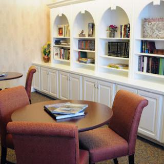A cozy study area featuring round tables, comfortable seating, and illuminated bookshelves.
