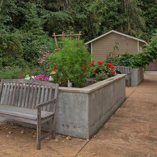 A serene garden setting featuring a wooden bench next to a raised planter filled with vibrant flowers and greenery.