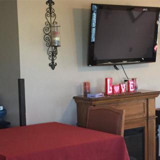 A cozy living room setup featuring a mounted television, a fireplace with decorative items, and a table with a red tablecloth.