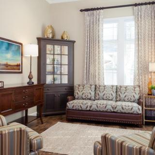 A cozy living room with a sofa, armchairs, and a wooden cabinet, featuring elegant curtains and soft lighting.