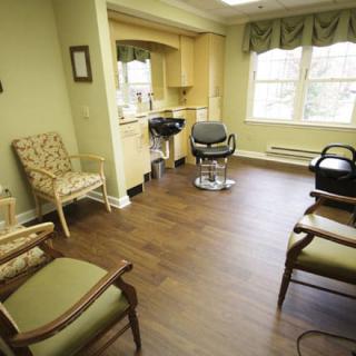 A cozy salon with several chairs and a hair styling station next to large windows.