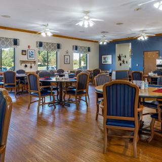 A spacious and well-lit dining area with multiple tables and chairs, featuring wooden floors and large windows.