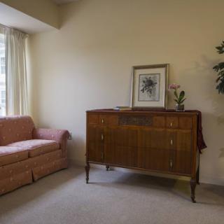 A cozy living room featuring a pink sofa, a wooden cabinet with decorative accents, and natural light filtering through the curtains.