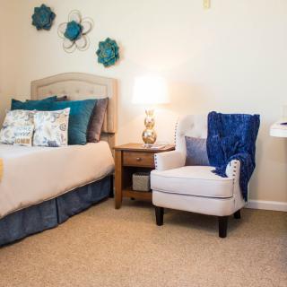 A cozy bedroom with a bed, a cushioned chair, and decorative accents.