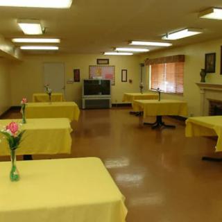 An empty dining room with tables covered in yellow tablecloths and decorated with flowers.