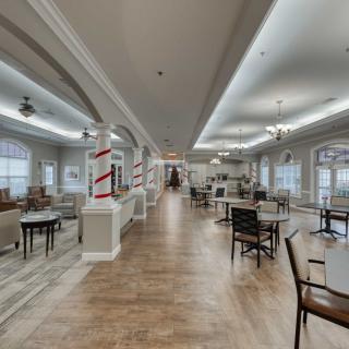 A spacious and well-lit dining area with wooden floors, arranged chairs and tables, and ceiling lights.