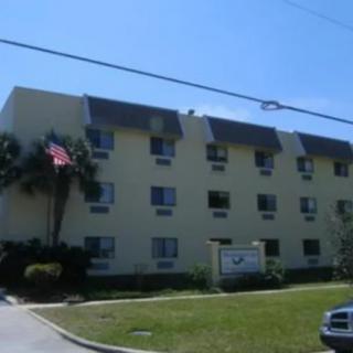 A three-story apartment building with a lawn, palm tree, and flag in front.