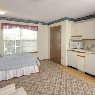 A cozy bedroom with a kitchenette, featuring a bed, microwave, and large window.