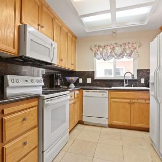 A well-lit kitchen with wooden cabinets, featuring modern appliances including a microwave, stove, dishwasher, and refrigerator.