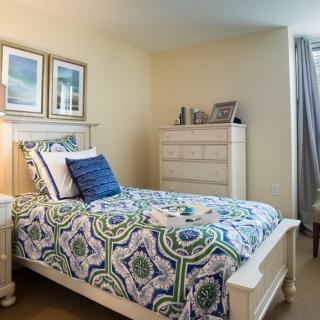 A cozy bedroom with a patterned bedspread, white furniture, and framed wall art.