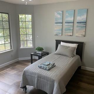 A minimalist bedroom with a single bed, large windows, and serene artwork on the wall.