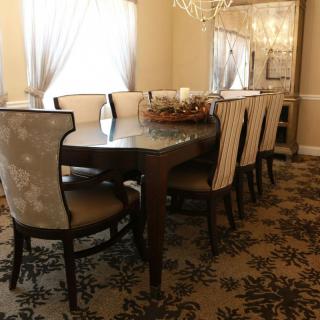 An elegantly decorated dining room featuring a large table with cushioned chairs, a chandelier, and patterned carpet.