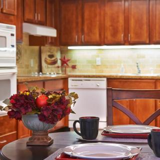 A cozy kitchen with wooden cabinets, a dining table set with plates and mugs, and a flower arrangement centerpiece.