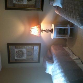 A cozy bedroom featuring twin beds, a nightstand with a lamp, and framed artwork on the wall.