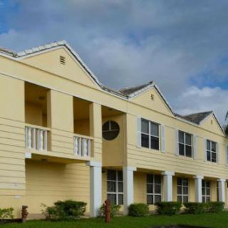 Yellow apartment complex with balconies and windows under a cloudy sky.