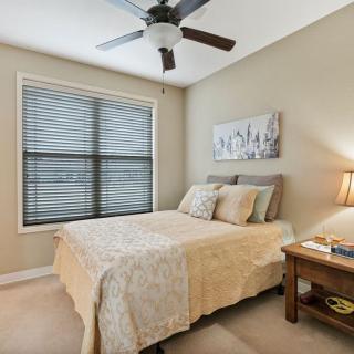 A cozy bedroom with a neatly made bed, ceiling fan, and a window with blinds.
