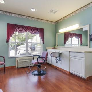 A well-lit hair salon interior with styling chairs, mirrors, and large windows adorned with drapes.