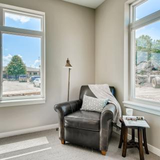 A cozy living room corner featuring a black leather armchair and a side table, bathed in natural light from large windows.