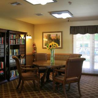 A cozy reading room with a table, chairs, and a bookshelf filled with books.