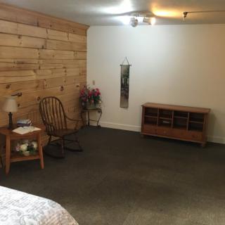 A cozy bedroom with a wooden accent wall, featuring a rocking chair, dresser, and decorative plant.