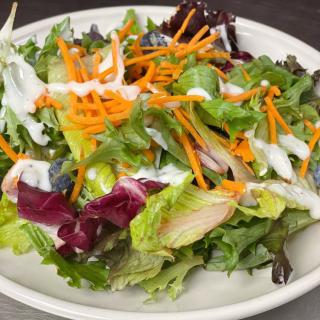 A fresh mixed green salad with shredded carrots and a drizzle of dressing.