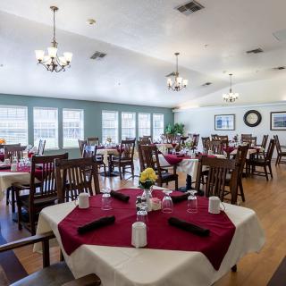 A spacious dining room with neatly arranged tables and chairs, adorned with chandeliers and large windows.