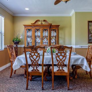 A classic dining room with a wooden table and intricately designed chairs, featuring a china cabinet in the background.