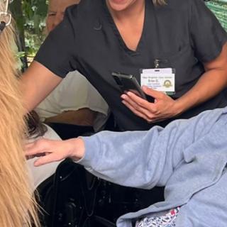 A caregiver interacting with an elderly person in a wheelchair outdoors.