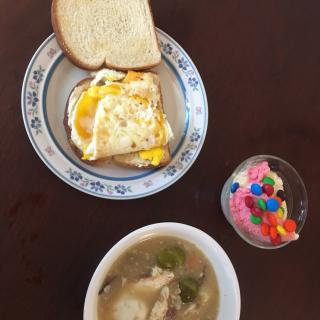 A breakfast meal featuring eggs and toast, a bowl of soup, and a colorful dessert.