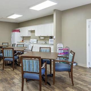 A kitchen and dining area with multiple tables and chairs, featuring appliances and ample lighting.