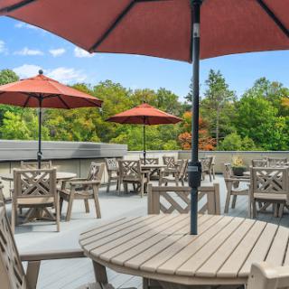 A peaceful outdoor patio area, featuring wooden tables and red umbrellas surrounded by lush greenery.