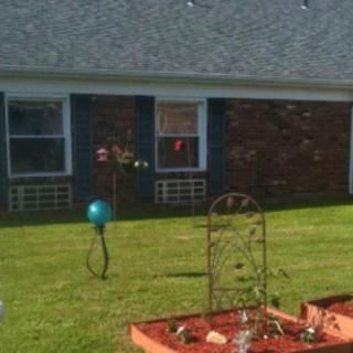 A well-maintained garden with flower beds and decorative elements in front of a brick house.