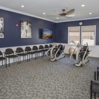 A fitness room with exercise machines, chairs lined up against the walls, and a television mounted on a navy blue wall.