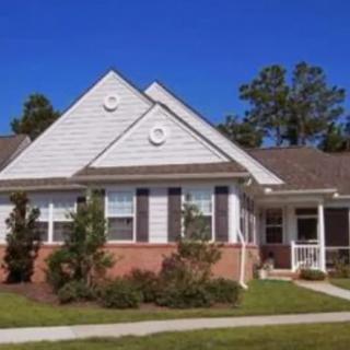 A suburban house with a brick and siding exterior, surrounded by well-maintained landscaping under a clear blue sky.