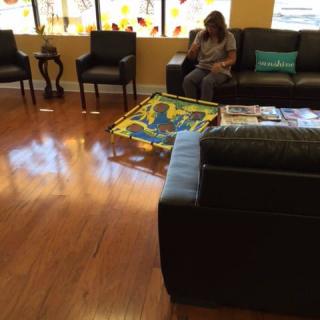 A waiting room with seating and a woman sitting on a couch.