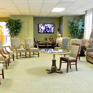 A waiting room with multiple chairs, a television on the wall, and decorative plants.