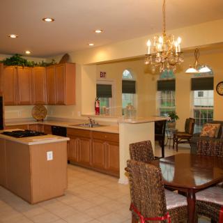 A spacious kitchen with an island counter and adjacent dining area, featuring wooden cabinets and a chandelier.