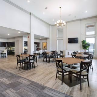 A modern, spacious dining area with multiple tables and chairs, featuring a high ceiling and a chandelier, bathed in natural light.